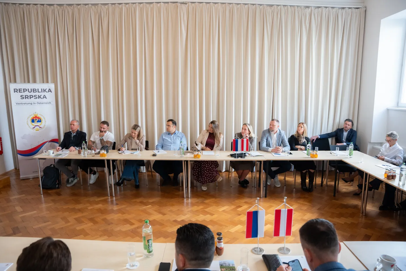 Die Teilnehmerrunde an der langen Tafel vor dem Aufsteller der Republika Srpska
