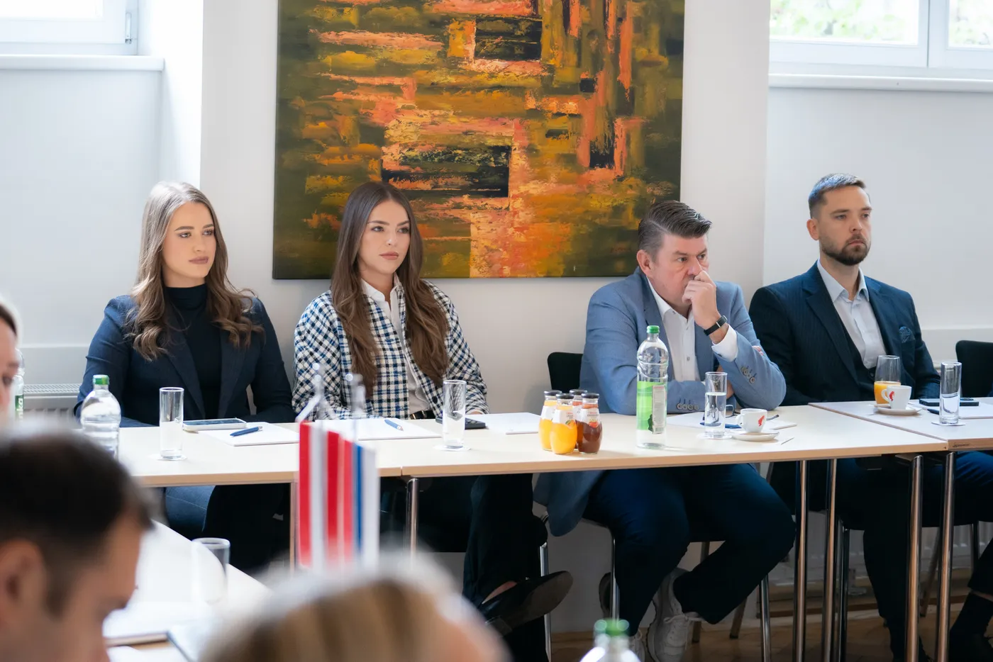 Vier Teilnehmer an der Tafel vor einem Gemälde im Saal