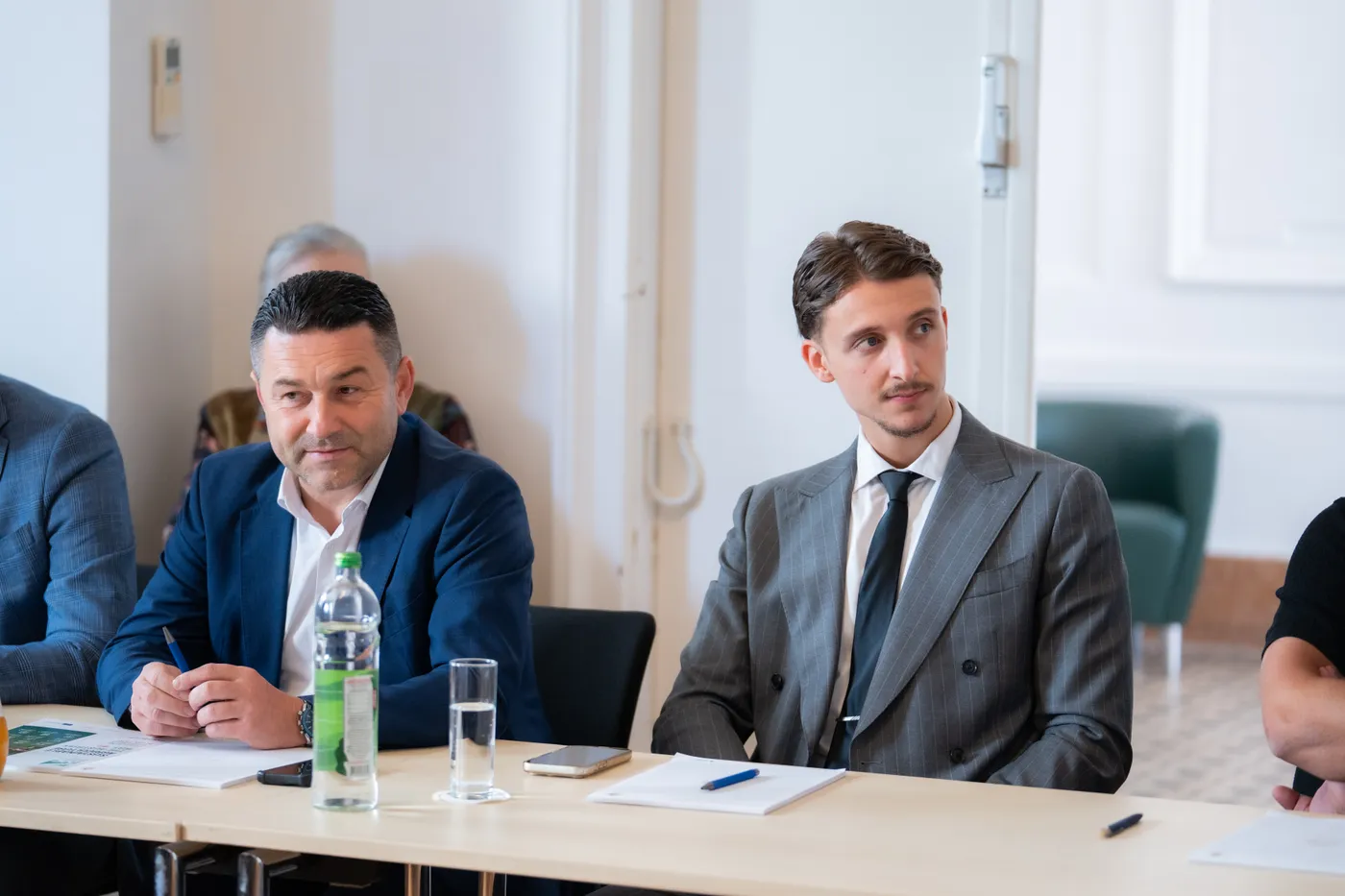 Zwei Teilnehmer mit Notizblock und Stift am Tisch