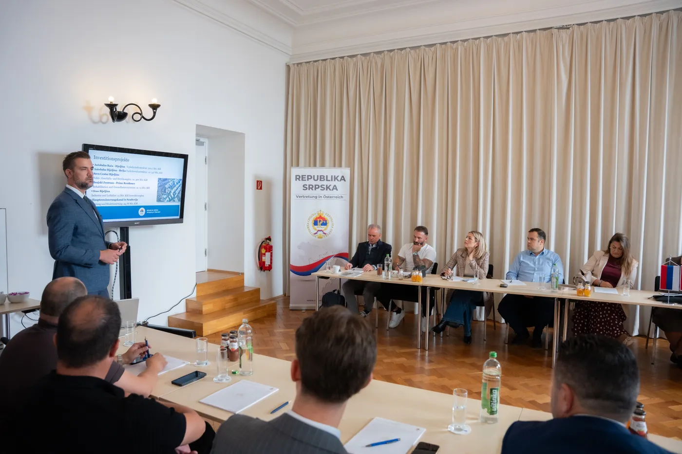 Folie zu Investitionsprojekten der Region, davor die Zuhörenden an der Tafel